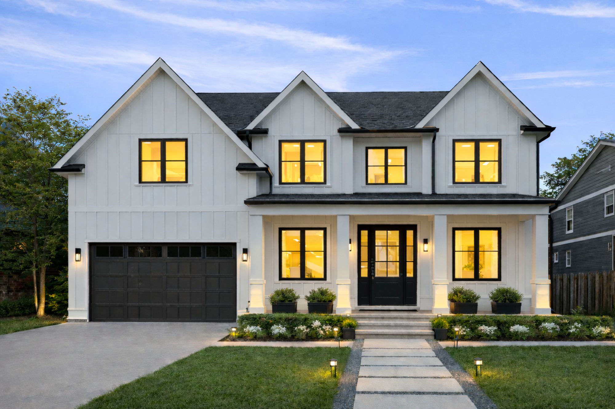 potomac elevation exterior by august homes white farmhouse style home with black windows and illuminated facade at dusk